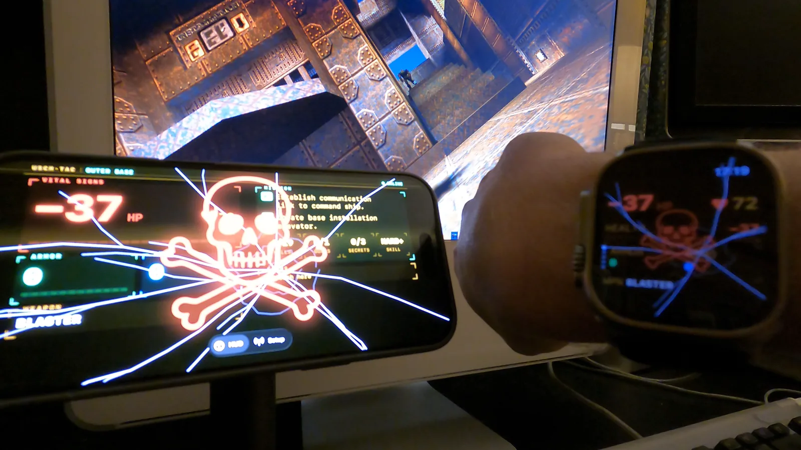 A 2005 iMac G5 running Quake II, an iPhone beside it and an Apple Watch on a wrist, all three screens showing the same cracked-glass red skull death overlay at -37 HP
