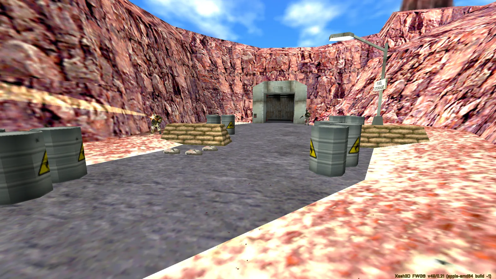 An outdoor canyon of red rock with hazard barrels and a bunker entrance under a blue sky